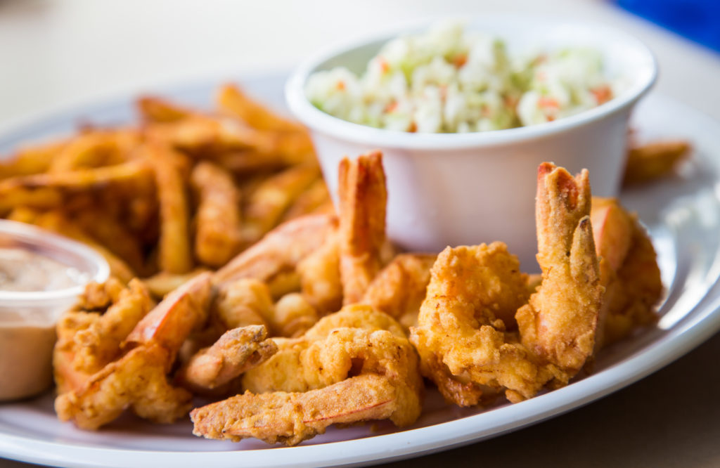 A fried shrimp dinner with french fries, coleslaw and sauce
