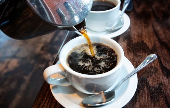 Fresh hot coffee being poured into a cup from a stainless steel french press in a trendy cafe